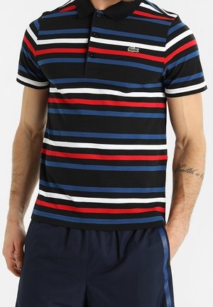 Man draagt een zwart poloshirt met horizontale rode, witte en blauwe strepen en donkerblauwe korte broek met een zijstreep.