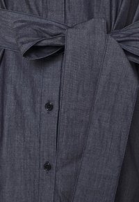 Tissu en denim gris foncé avec des boutons cousus et une large ceinture nouée en nœud papillon à la taille d'un vêtement.