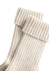 Skarpetki z kremowego, prążkowanego wełnianego materiału z zagiętymi mankietami, pokazane z bliska na białym tle.