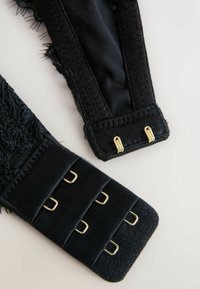 Black lace bra straps show textured fabric with frayed edges, alongside a flat strap featuring four gold metal loops for adjustment.