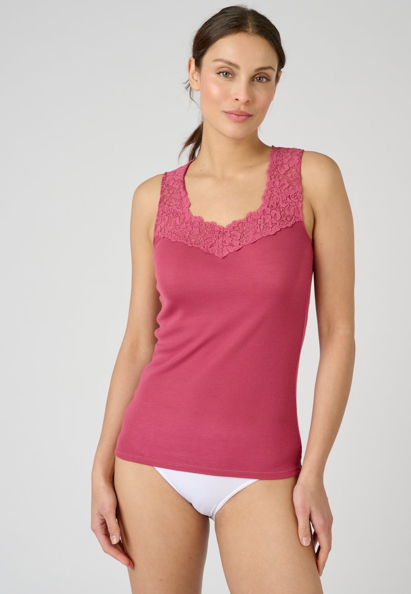 Top tank rosa aderente con colletto in pizzo testurizzato, design senza maniche e tessuto morbido. Abbinato a biancheria intima bianca.