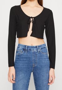 Svart ribbad långärmad crop top med rund halsringning och frontknut. Kombinerad med högmidjade blå jeans med klassisk passform.