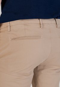 Pantalones de algodón beige con una textura suave, que presentan una cinturilla limpia, un bolsillo trasero con una abertura estrecha y detalles de costura sutiles.