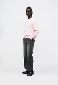 Ροζ ανοιχτόχρωμο φούτερ με μακριά μανίκια, γκρι τζιν με ίσια γραμμή και σκούρα παπούτσια τύπου slip-on. Απλός σχεδιασμός με χαλαρή εφαρμογή και ριμπ μανσέτες.