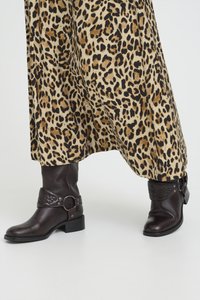 Brown leather ankle boots with a short block heel, featuring a decorative strap and buckle, paired with a leopard print skirt.