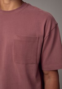 T-shirt a maniche corte, con collo a giro, di colore mauve smorzato, realizzato in tessuto morbido, con taschino sul lato sinistro del petto con cuciture precise.