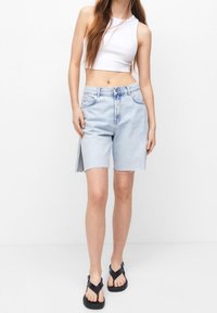 Shorts de denim azul claro con corte recto, dobladillo deshilachado y aperturas laterales. Combinados con sandalias negras y una camiseta cortada blanca.