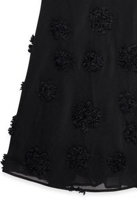 Robe noire en tissu texturé, ornée d'appliqués floraux en 3D regroupés. L'ourlet est légèrement transparent, ajoutant de la profondeur au design.