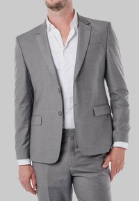 Costume gris en tissu lisse, comprenant une veste à boutonnage simple, des revers en crans et un pantalon assorti. Une chemise blanche est portée en dessous.