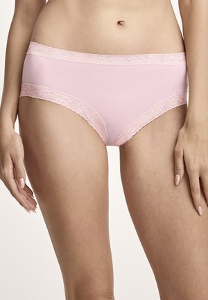 Woman wearing light pink lace-trimmed cotton briefs, standing with hands relaxed by her sides against a plain background.