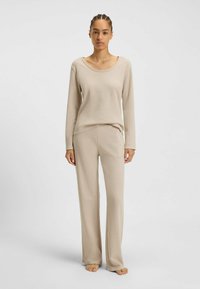 Beige långärmad topp och matchande vida byxor i textil med struktur, med rundad halsringning och avslappnad passform.