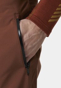 Bruine stoffen broek met een zijzak met rits en een zwarte ritsdetail. De pols heeft een gestructureerde, roodbruine stof met een gouden streep.