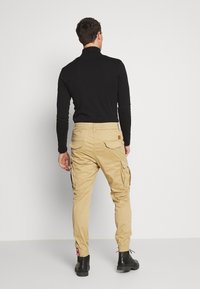 Beige cargobyxor med sidfickor, elastiska muddar och en brun lapp på bältet bak. Bärs med en svart långärmad topp och svarta stövlar.