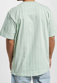 Miętowo-zielona koszulka z luźnym krojem, krótkimi rękawami i pionowymi białymi paskami. Miękki bawełniany materiał z gładkim tyłem.