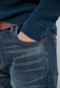 Donkerblauwe gebreide trui met ribbeltextuur, gecombineerd met vervaagde denim jeans met oranje stiksel en een zak.
