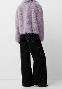 Fluffy lavendel faux fur jakke med cropped design, kombineret med højtaljede sorte vidde bukser med sølvnitter langs sømmene.