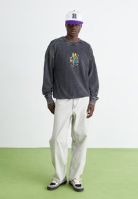 Grijze, oversized sweatshirt met een kleurrafische grafiek in het midden, gecombineerd met lichte, ruime jeans en zwarte, roze en witte sneakers.