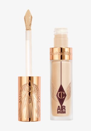 Liquid concealer with a gold accent applicator and a clear container. Product features a printed logo and decorative wings design.