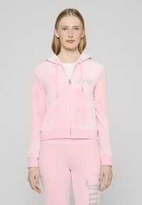 Rózsaszín, lágy velúr anyagból készült cipzáras kapucnis pulóver, melynek bal mellrészén fehér, strasszos logó található, és elasztikus mandzsettákkal rendelkezik.