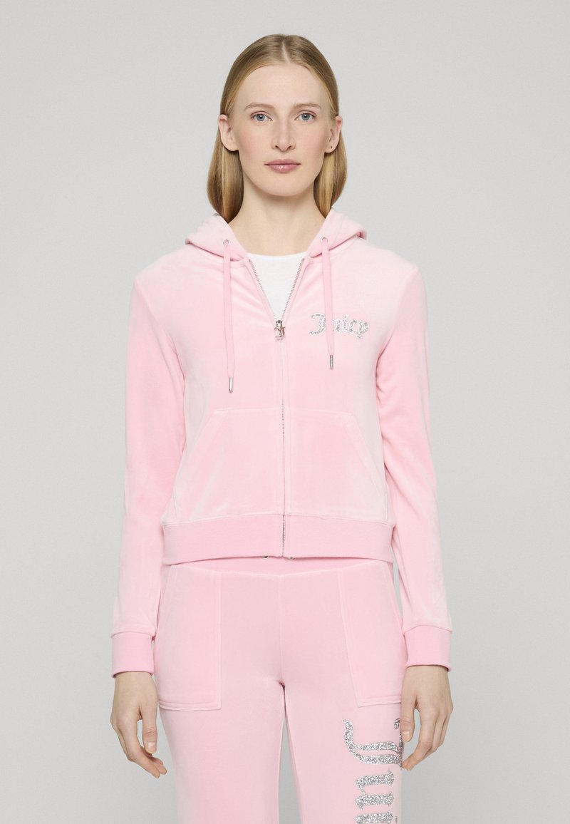 Rózsaszín, lágy velúr anyagból készült cipzáras kapucnis pulóver, melynek bal mellrészén fehér, strasszos logó található, és elasztikus mandzsettákkal rendelkezik.