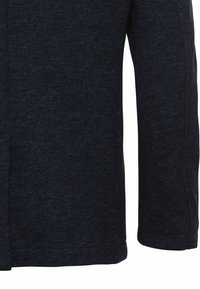 Manche de manteau en tissu texturé bleu foncé avec coutures apparentes et une coupe structurée, ajustée.