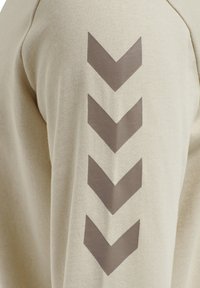 Felpa beige con finitura testurizzata e motivo a zigzag marrone sulla manica. Tessuto a trama stretta con dettagli a costine sui polsini.