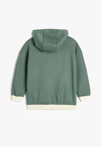 Sudadera verde con capucha, puños y cinturilla de canalé blancos. Tejido suave con un corte holgado, sin patrones ni adornos visibles.