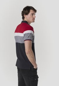Polo à blocs de couleurs avec des panneaux rouges, blancs, gris et bleu marine. Manches courtes et col classique. Tissu en coton texturé.