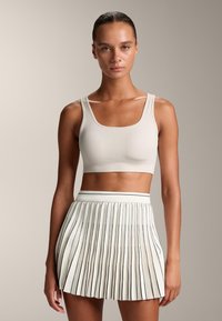 Beige randig crop top med fyrkantig halsringning som matchas med en plisserad vit kjol med svarta ränder. Slät textur med en åtsittande design.