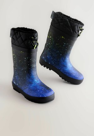 Bottes de pluie en caoutchouc avec un motif galaxie bleu, un revers matelassé noir et des accents verts. Elles sont dotées d'une semelle noire texturée pour une meilleure adhérence.