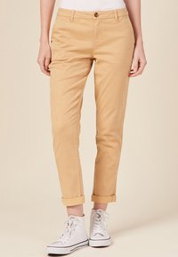 Beige katoenen chinos met een slim fit, voorzien van een enkele knoopsluiting, opgerolde mouwen en zijzakken. Gecombineerd met witte hoge sneakers.