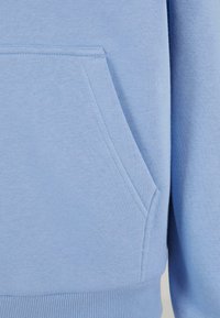 Felpa blu con tasca a marsupio frontale, polsini e orlo a coste; texture morbida con una finitura liscia e dettagli di cucitura minimi.