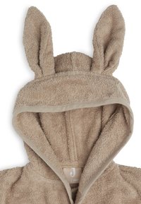 Robe en serviette beige doté d'une capuche avec des oreilles de lapin, texture en éponge douce et bordure contrastante autour de la capuche et de l'ouverture avant.