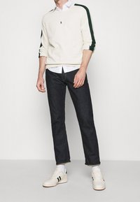 Krémový svetr se zelenými pruhy, žebrované manžety, doplněný tmavými džínami a bílými teniskami se zelenými akcenty. Ležérní outfit.