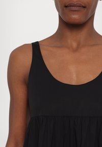 Mustat hihattomat mekko, jossa on pyöreä kaula-aukko ja rypistetty yläosa, joka tarjoaa rentoa istuvuutta. Sileä kankaan rakenne, minimalistinen muotoilu.