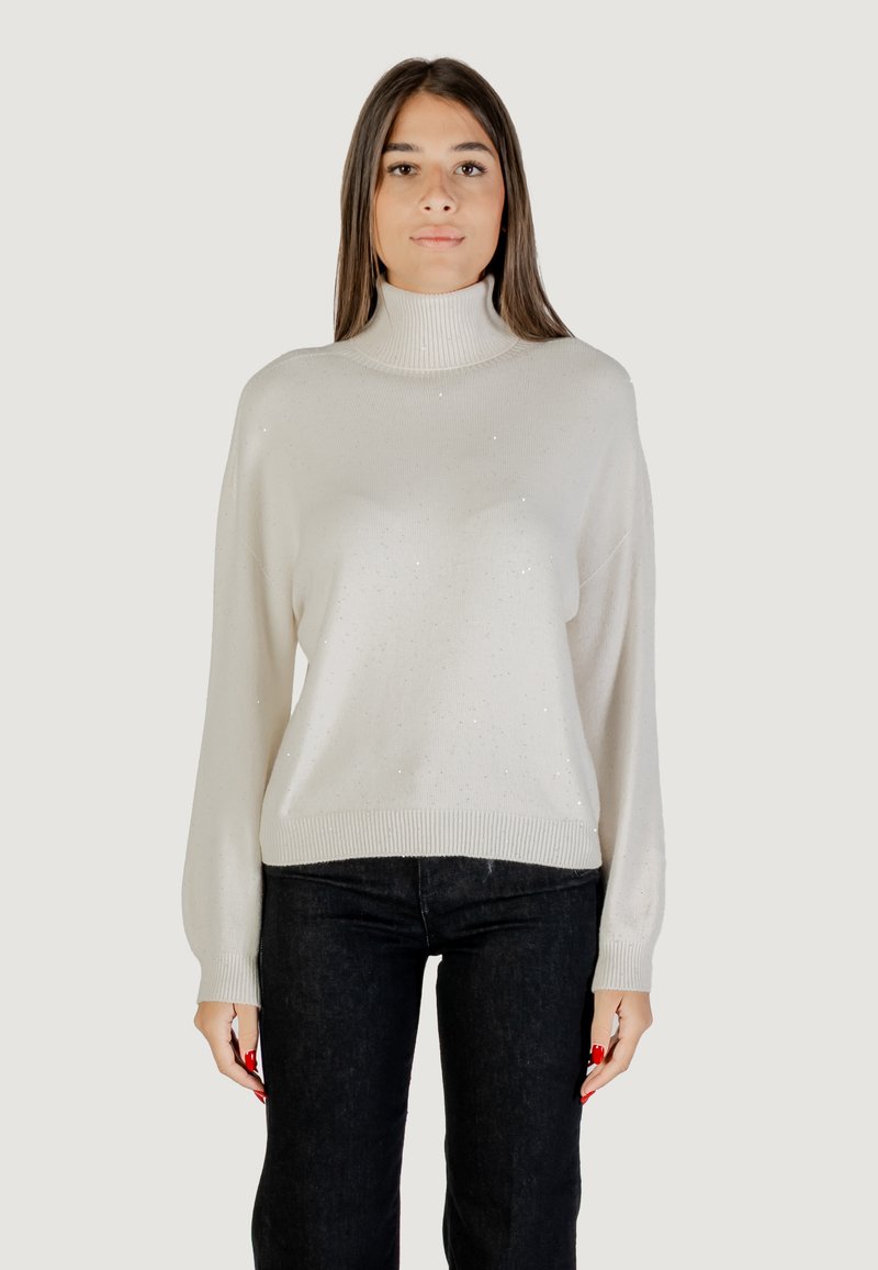 Pull à col roulé blanc avec une coupe décontractée, mettant en avant un tricot texturé et de subtils accents de paillettes. Associé à un jean foncé.