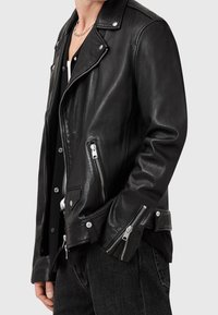 Giubbotto motociclistico in pelle nera con zip asimmetrica, hardware argentato, tasche con zip e silhouette aderente. Texture liscia.