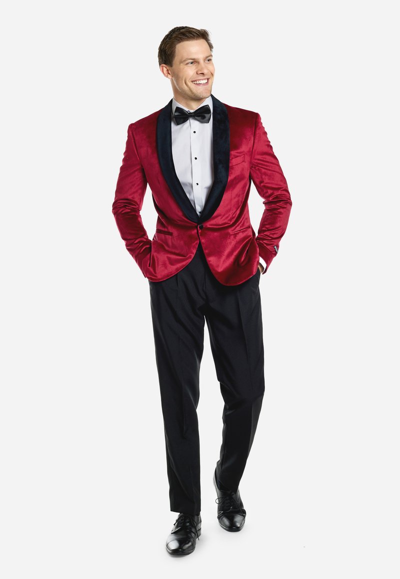 Rotes Samt-Smokingjackett mit schwarzen Satin-Revers, kombiniert mit einem weißen Hemd, einer schwarzen Fliege und schwarzen Hosen. Schwarze formelle Schuhe.