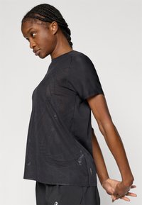 Μαύρο αθλητικό t-shirt με διαπνέον σχέδιο από δίχτυ, κοντά μανίκια και διακριτικά γεωμετρικά μοτίβα, προσφέροντας άνετη εφαρμογή.