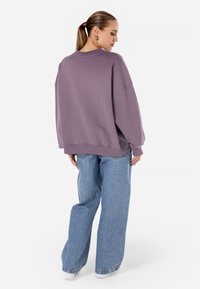 Felpa oversized lavanda con spalle scese, polsini e orlo a coste, abbinata a jeans a gamba larga blu chiaro. Tessuto dalla superficie liscia.