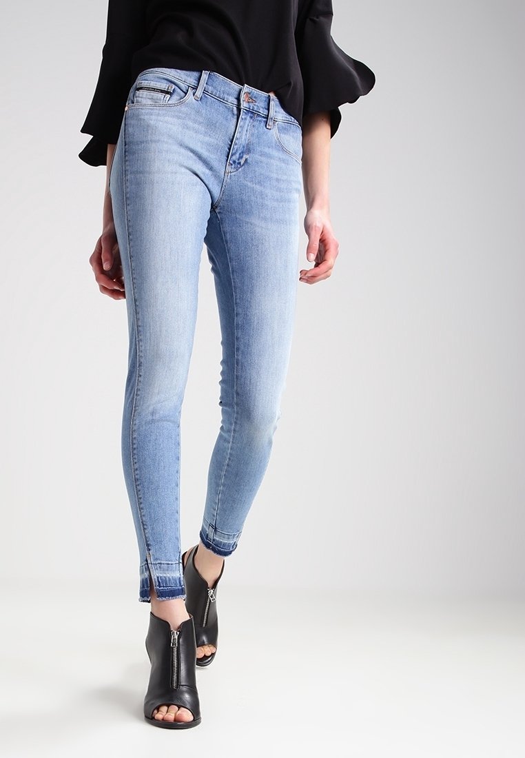 Ljust blå skinny jeans med en urtvättad look, hög midja, ankelsiddragkedjor och en tight passform, kombinerat med svarta öppna stövletter.