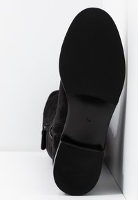 Botín negro de ante con punta redonda, suela de goma plana, cremallera lateral y detalles texturizados en la parte superior.