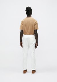 Lysebrun bomulds-T-shirt og hvide hørbukser set bagfra, med afslappet pasform, lige snit og let tekstur. Brune slip-on sko fuldender outfit.