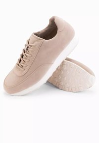 Beige mockaskor med rund tå, snörning och en vit gummisula med ett strukturerat mönster p�å undersidan.