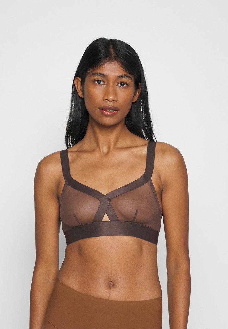 Bralette de malla marrón con tirantes gruesos y un diseño entrelazado. Textura suave, cobertura mínima y un detalle de ojo de cerradura en el centro.