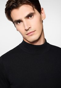 Czarny prążkowany sweter z golfem o dopasowanym kroju i teksturowanej tkaninie, z wysokim kołnierzem, który ciasno oplata szyję.