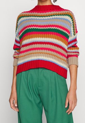 Pull en maille à rayures horizontales rouges, vertes, beige, bleues et oranges, associé à un pantalon vert taille haute, visible des épaules aux hanches.