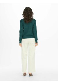Maglione verde lavorato a maglia con scollatura rotonda, abbinato a pantaloni bianchi a gamba larga. Tessuto con texture e polsini a coste. Sandali neri con tacco.