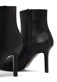 Bottines noires en cuir lisse, dotées d'une fermeture éclair sur le côté et de talons fins et hauts. Le design comprend une pointe effilée et peu de détails.
