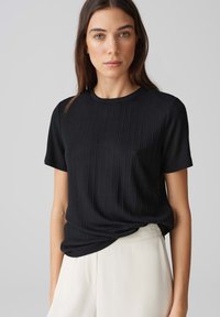 Zwarte ribbelige t-shirt met korte mouwen en een ronde halslijn, met een zachte textuur. Gecombineerd met lichte broek.